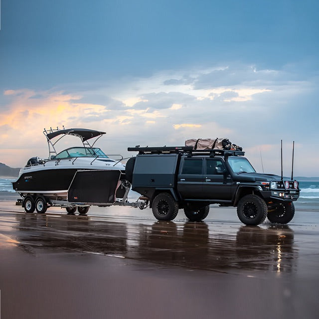 Black boat being towed by 4WD on the beach at sunset